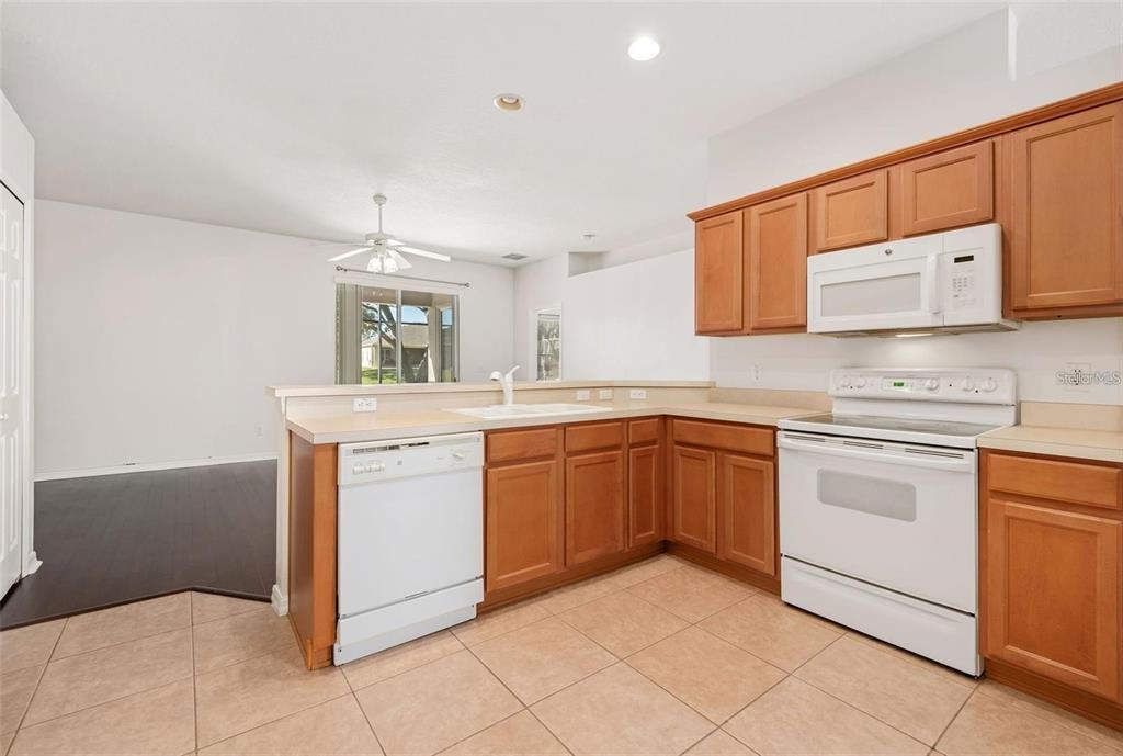 A kitchen with wood cabinets, white appliances, and tile flooring opens to a living area — 9651 OLD MARSH COURT, ORLANDO, FL