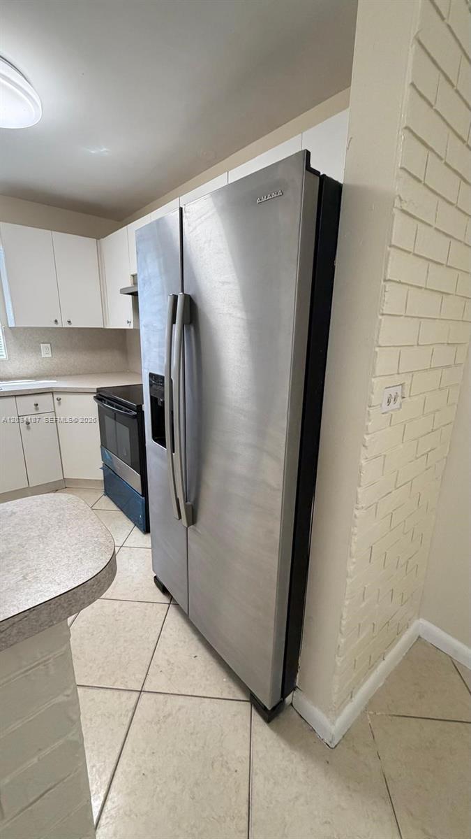 A kitchen features a stainless steel Amana refrigerator, white cabinets, and light-colored tile flooring — 1130 NW 43rd Ter # 0, Lauderhill FL 33313, LAUDERHILL, FL