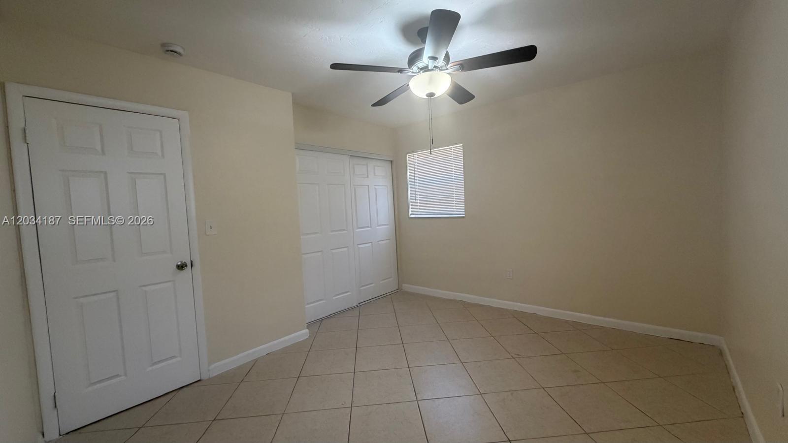 An empty room features beige walls, tiled floors, a ceiling fan, and two white doors — 1130 NW 43rd Ter # 0, Lauderhill FL 33313, LAUDERHILL, FL
