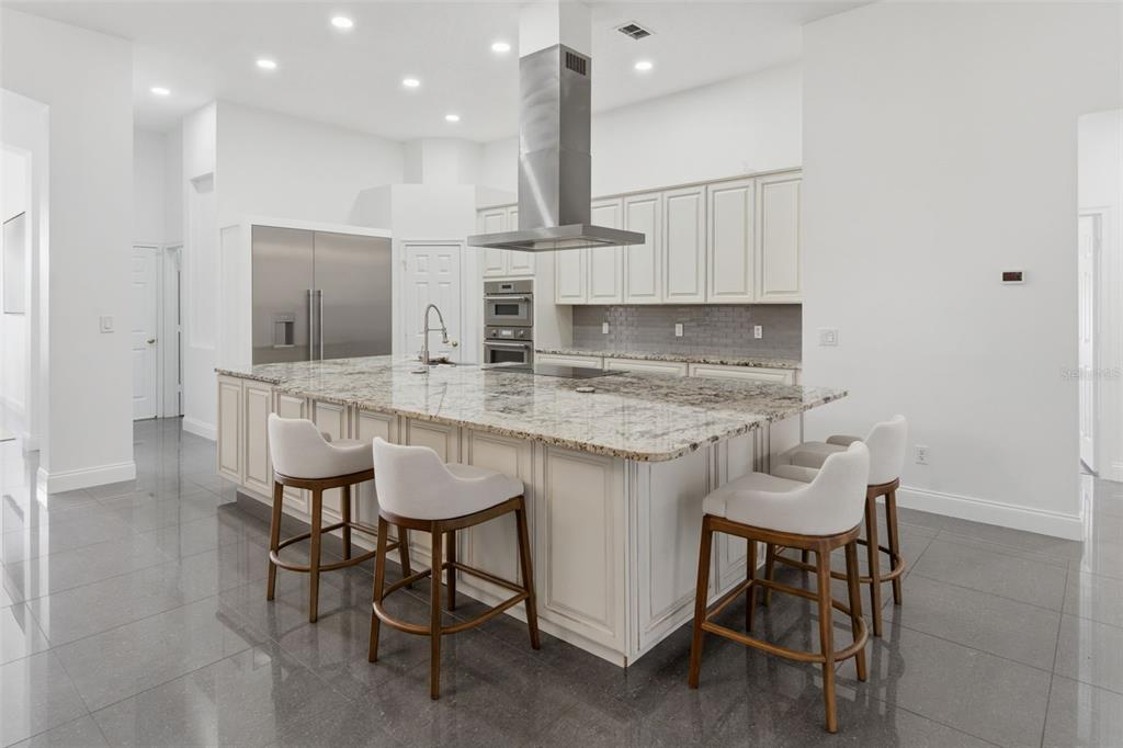 A modern kitchen features a large granite-topped island, stainless steel appliances, and white cabinetry — 12513 SCARLETT SAGE COURT, WINTER GARDEN, FL
