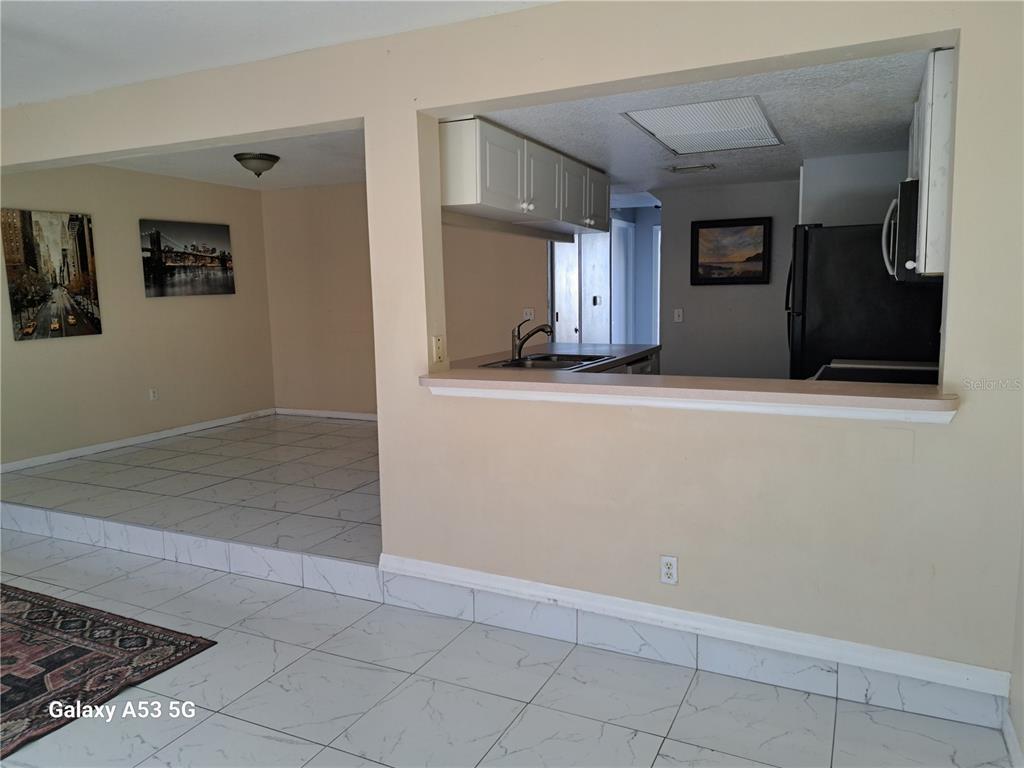 A kitchen with white cabinets and a pass-through window overlooks a tiled living area — 153 MANGO DRIVE, DAVENPORT, FL
