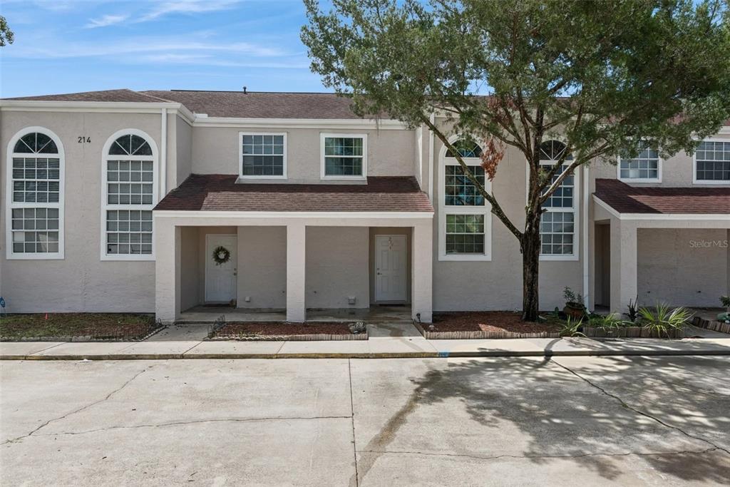 An exterior view of a two-story townhouse complex with beige stucco walls and arched windows — 214 MAJORS LANE UNIT C, KISSIMMEE, FL