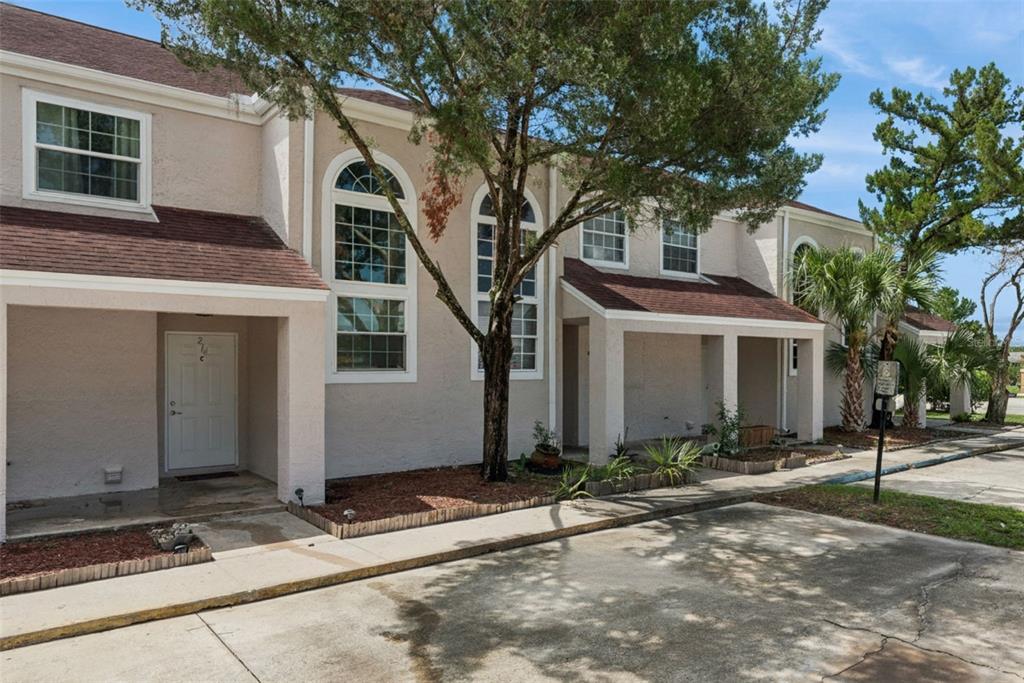 A two-story townhouse exterior features beige stucco walls, brown shingled roofs, and arched windows — 214 MAJORS LANE UNIT C, KISSIMMEE, FL