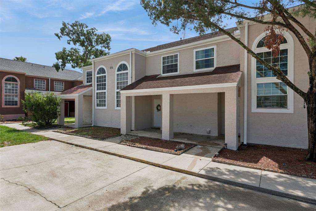 A two-story beige townhouse with a covered front porch and arched windows under a blue sky — 214 MAJORS LANE UNIT C, KISSIMMEE, FL