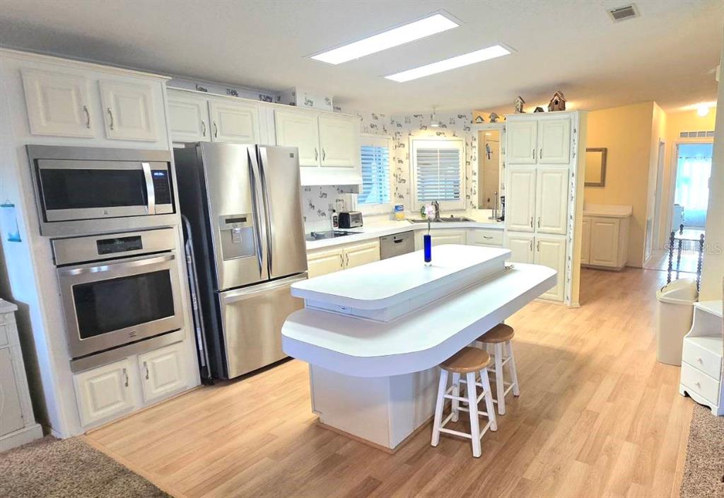 A kitchen features white cabinetry, stainless steel appliances, a tiered island, and light wood flooring — 31 REVERE WAY UNIT 23, PALM HARBOR, FL