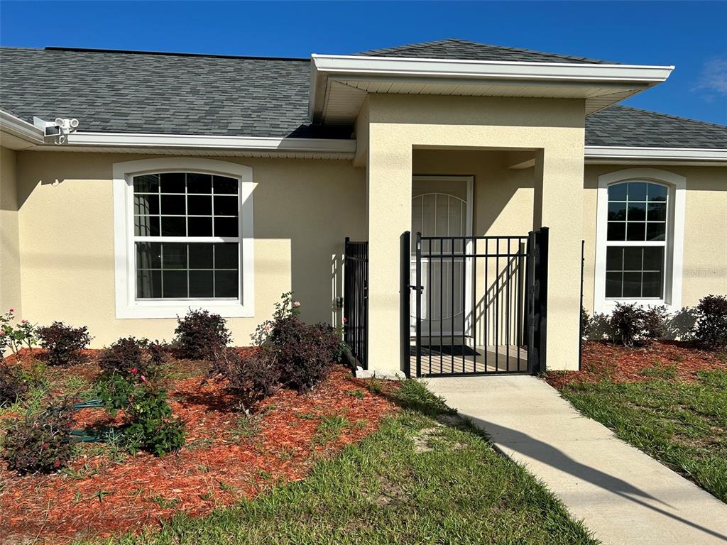 The exterior of a beige house features a gated entryway, a walkway, and landscaped bushes — 16750 SW 18TH AVENUE ROAD, OCALA, FL