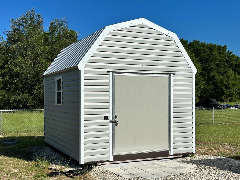A light gray barn-style storage shed sits on a gravel pad in a grassy yard — 16750 SW 18TH AVENUE ROAD, OCALA, FL