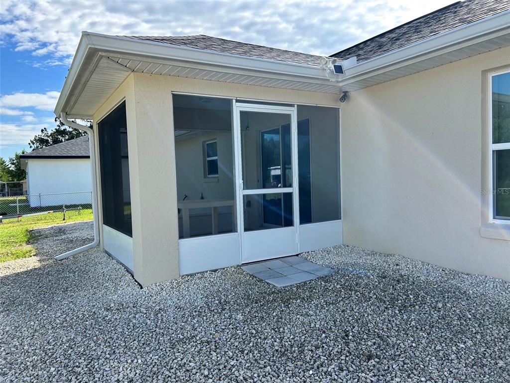 A screened-in porch with a white door sits on a gravel yard next to a house — 16750 SW 18TH AVENUE ROAD, OCALA, FL