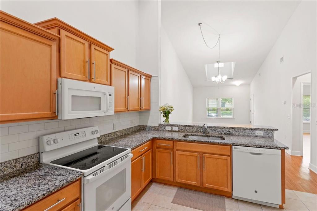 A kitchen with light wood cabinets, granite countertops, white appliances, and a high vaulted ceiling — 2242 NW 51ST AVENUE, GAINESVILLE, FL