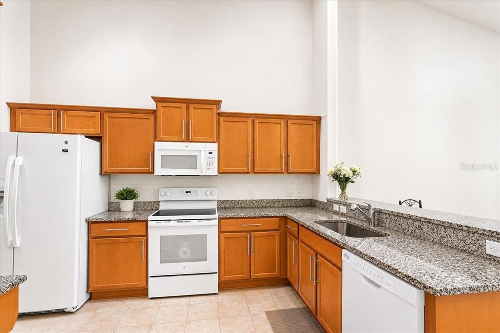 A kitchen features wood cabinets, granite countertops, white appliances, and a tile floor — 2242 NW 51ST AVENUE, GAINESVILLE, FL