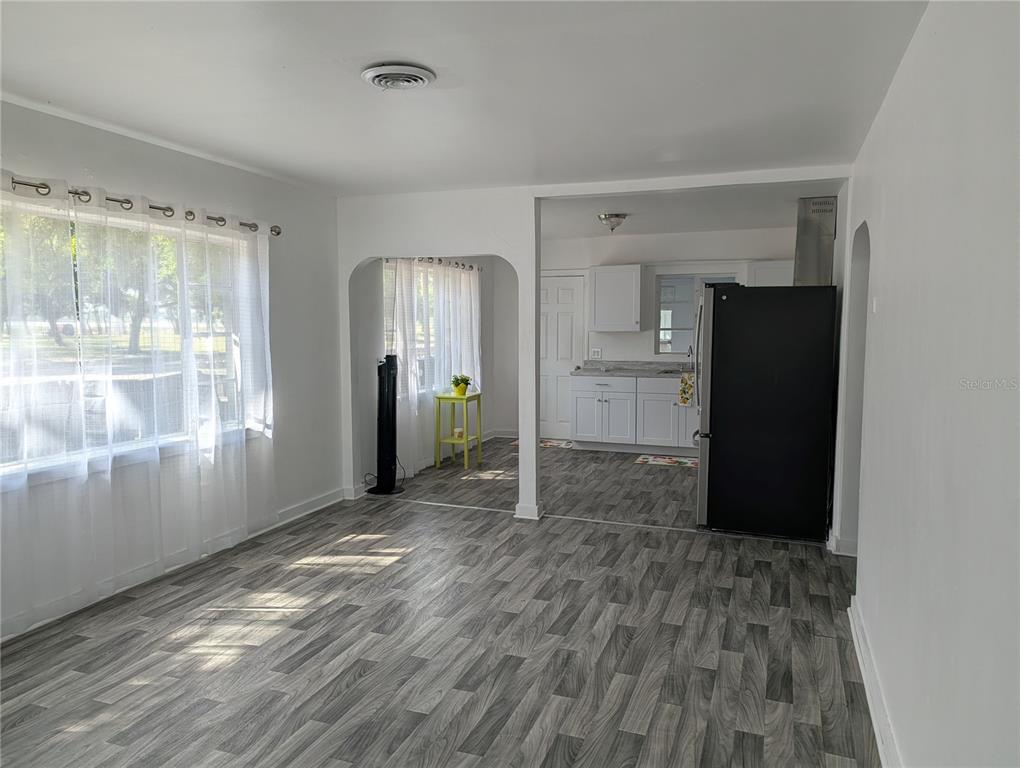 A living area with gray wood-look flooring leads into a kitchen with white cabinets — 3834 DR MARTIN LUTHER KING JR STREET S, ST PETERSBURG, FL