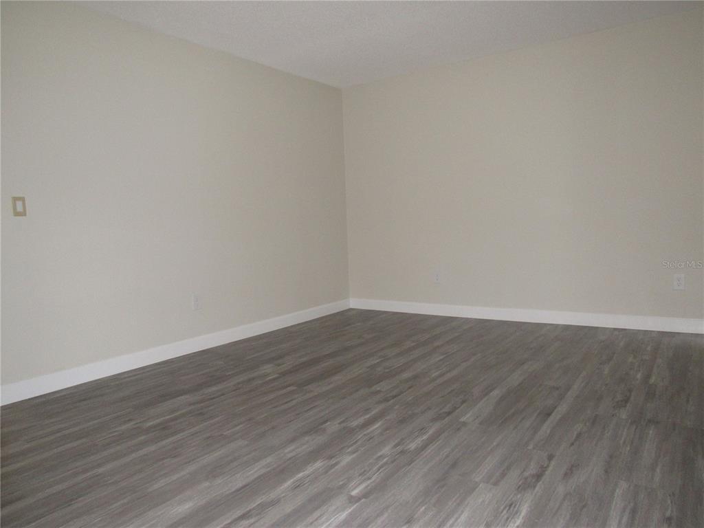 An empty room features light-colored walls, white baseboards, and gray wood-look flooring — 22333 EDGEWATER DRIVE UNIT D-5, PUNTA GORDA, FL