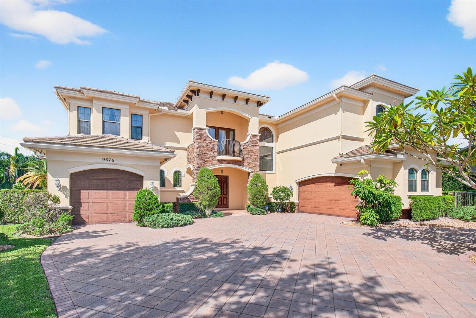 A two-story stucco house features a stone-accented entryway, a balcony, and two garage doors — 9576 Equus Circle, Boynton Beach FL 33472, BOYNTON BEACH, FL