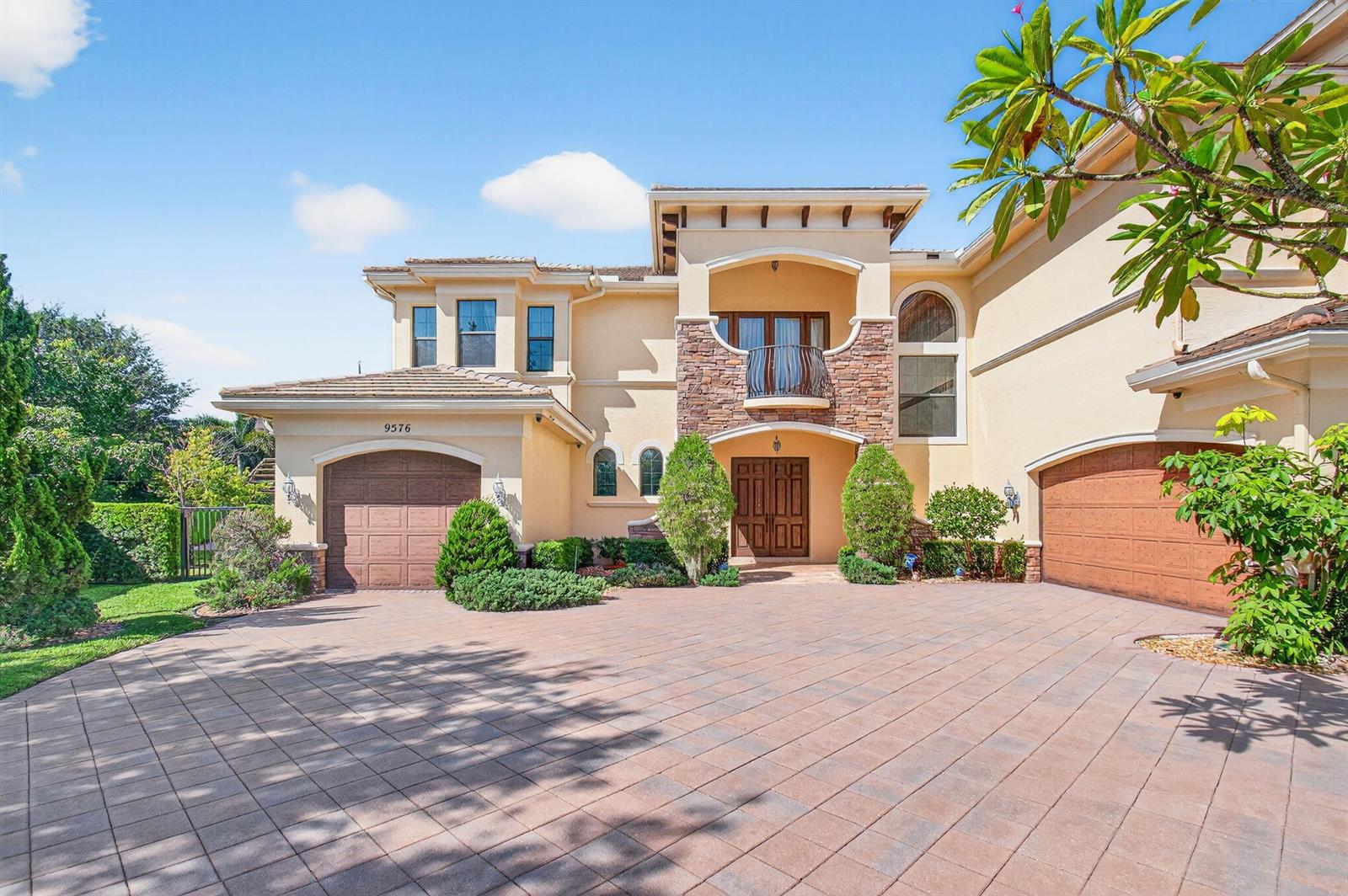 A two-story stucco house features a stone-accented entrance, a balcony, and two garage doors — 9576 Equus Circle, Boynton Beach FL 33472, BOYNTON BEACH, FL