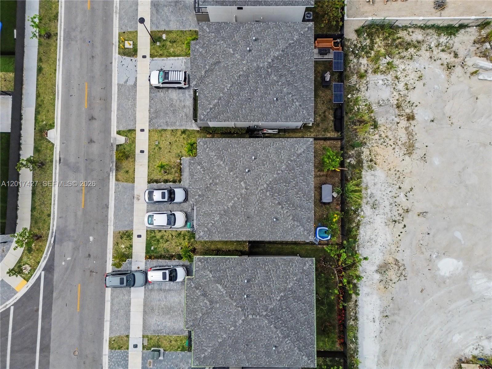 An aerial view shows three houses with gray roofs, driveways, and backyards bordering a dirt lot — 227 NW 13th Pl, Florida City FL 33034, FLORIDA CITY, FL