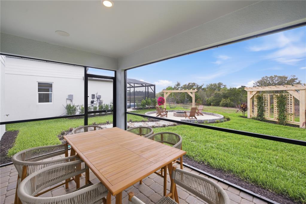 A screened-in patio features a dining set overlooking a backyard with a fire pit area — 805 BALLEBY TRAIL, BRADENTON, FL