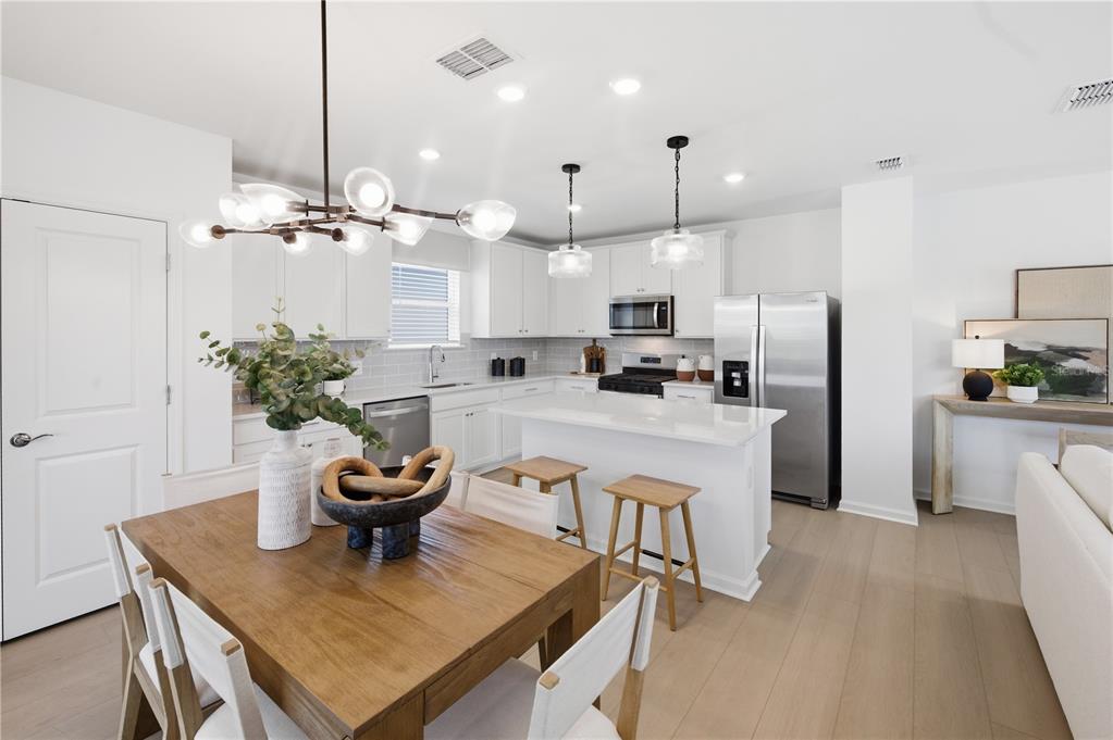 A modern kitchen with white cabinetry, a central island, and an adjacent dining area — 805 BALLEBY TRAIL, BRADENTON, FL