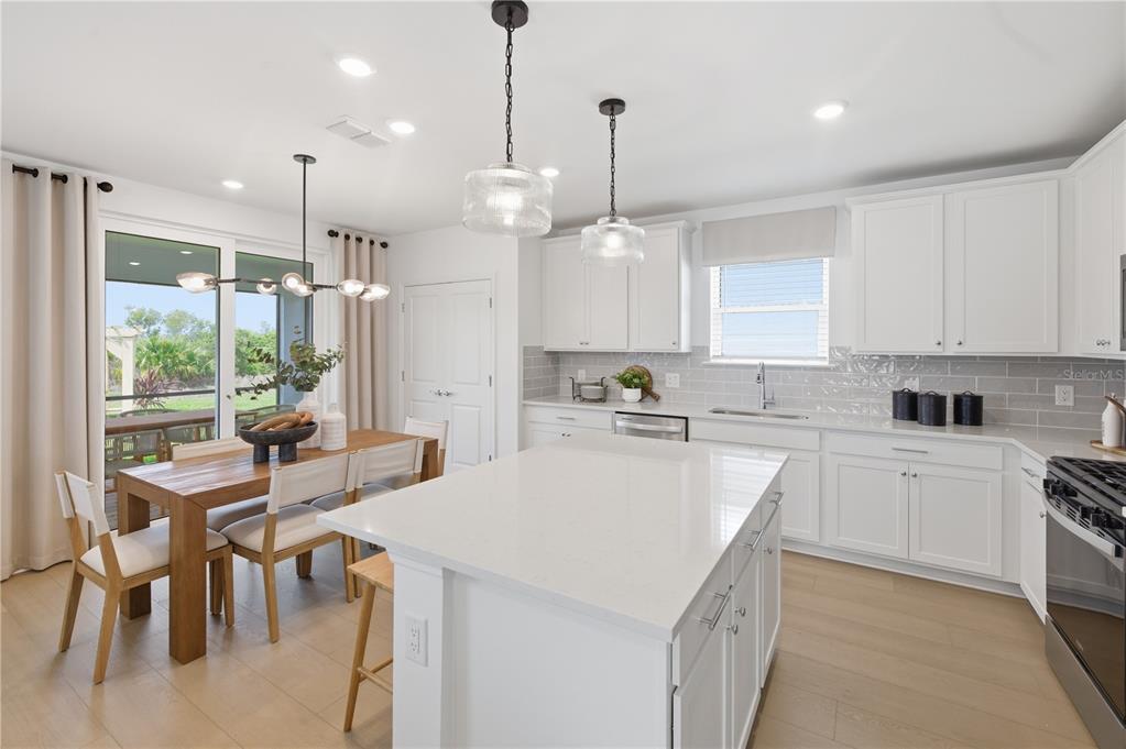 A bright kitchen features white cabinets, a quartz island, and an adjacent dining area — 805 BALLEBY TRAIL, BRADENTON, FL