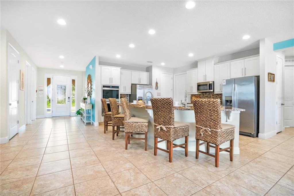 A kitchen with white cabinets, stainless steel appliances, and a breakfast bar with woven chairs — 7734 GRABEN STREET, KISSIMMEE, FL