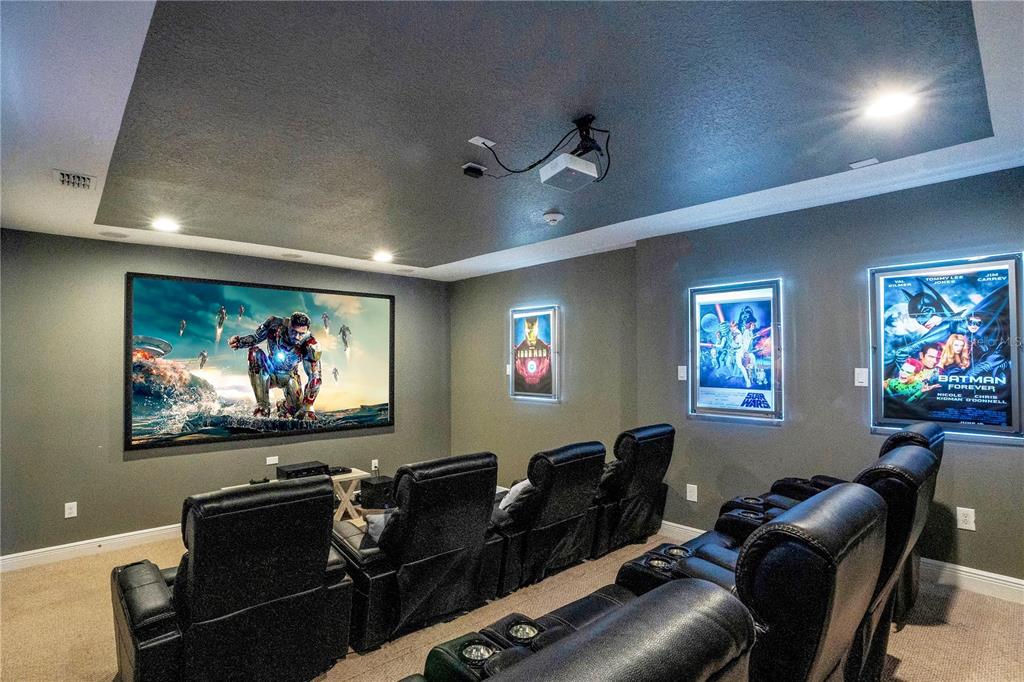 A home theater features a large projector screen, tiered leather seating, and illuminated movie posters — 7734 GRABEN STREET, KISSIMMEE, FL