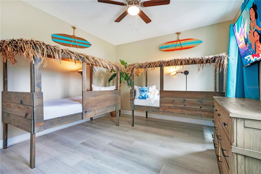 A bedroom features two wooden canopy beds with thatched roofs, surfboard wall decor, and light flooring — 7734 GRABEN STREET, KISSIMMEE, FL