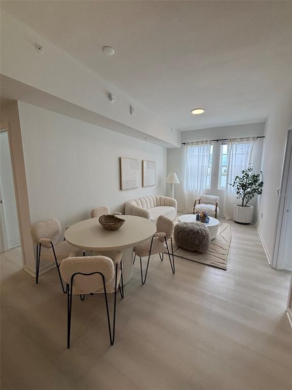 A bright, open-concept dining and living area features light wood flooring and neutral furniture — 5579 MILLENIA PARK UNIT 409, ORLANDO, FL