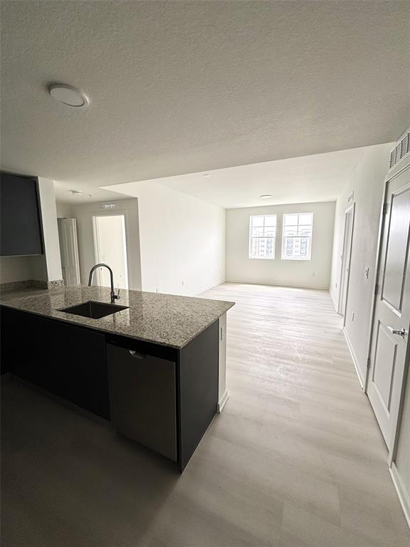 A kitchen island with a sink and dishwasher faces an open-concept living area with windows — 5579 MILLENIA PARK UNIT 409, ORLANDO, FL