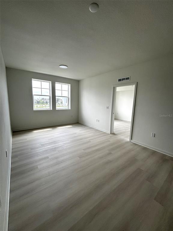 An empty room with light wood-look flooring, two windows, and a doorway to another room — 5579 MILLENIA PARK UNIT 409, ORLANDO, FL