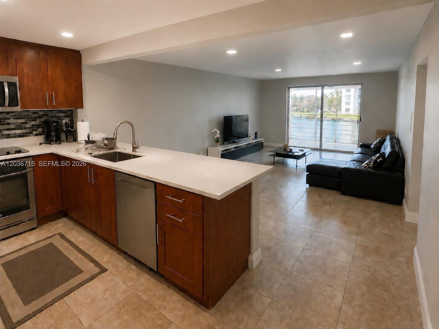 An open-concept kitchen with wood cabinets and a living area overlooking a waterfront balcony — 301 SE 3rd St # 204, Dania Beach FL 33004, DANIA BEACH, FL
