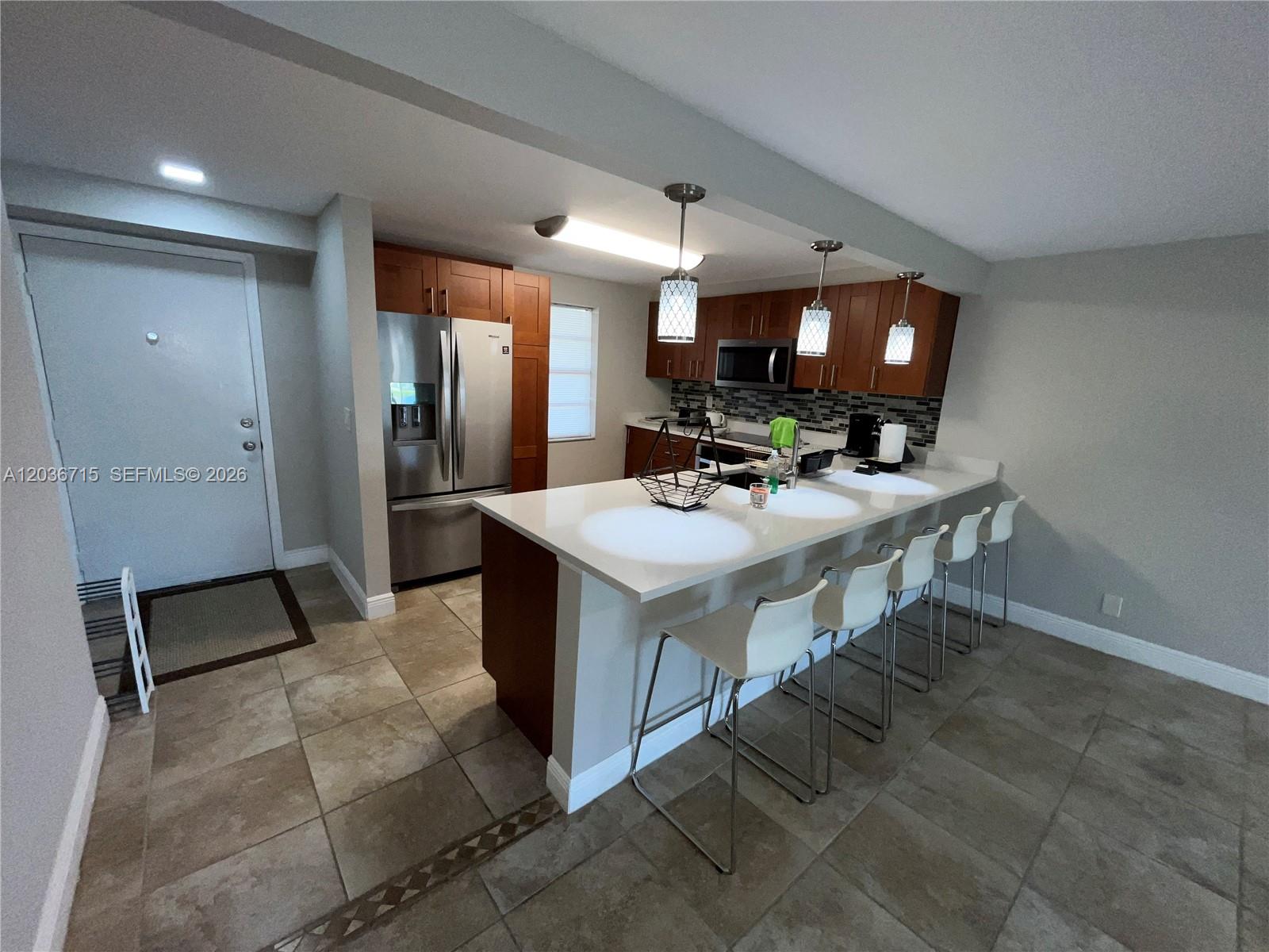 A kitchen features wood cabinets, stainless steel appliances, a white island, and tile flooring — 301 SE 3rd St # 204, Dania Beach FL 33004, DANIA BEACH, FL