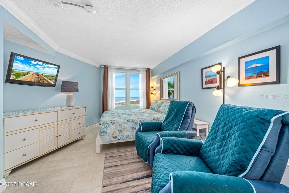 A bedroom features a bed, two blue armchairs, a dresser, and a view of the ocean — 2301 S ATLANTIC AVENUE UNIT 201, DAYTONA BEACH, FL