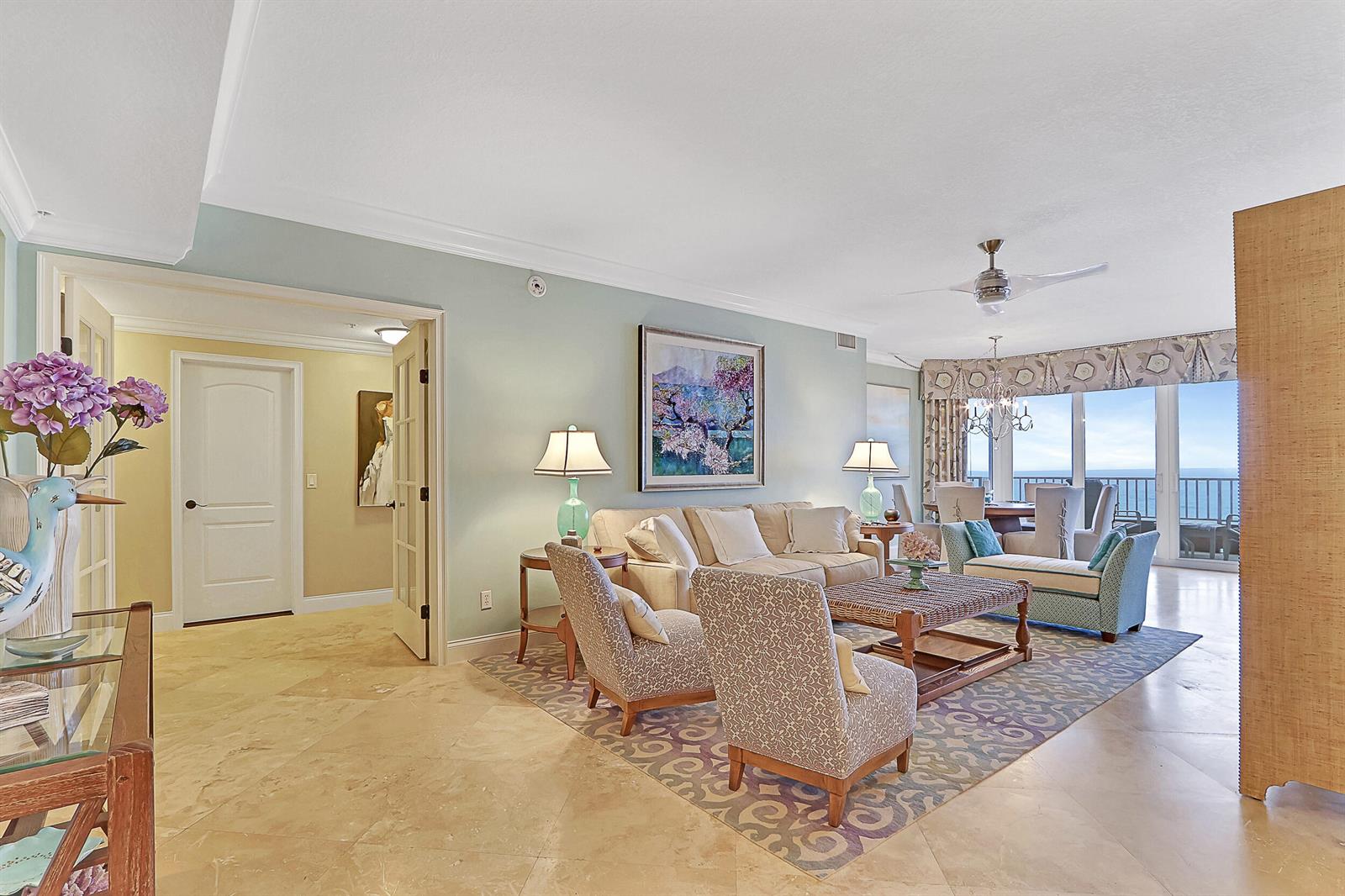 A living room with light blue walls, tile floors, patterned armchairs, and a balcony view — 750 Ocean Royale Way # 1203, Juno Beach FL 33408, JUNO BEACH, FL