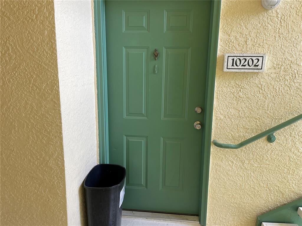 A green front door with a trash can sits next to a yellow stucco wall — 8820 DUNES COURT UNIT 202, KISSIMMEE, FL