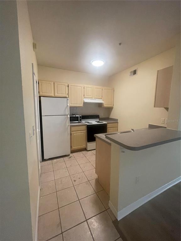 A kitchen features light wood cabinets, white appliances, a tiled floor, and a breakfast bar — 8820 DUNES COURT UNIT 202, KISSIMMEE, FL
