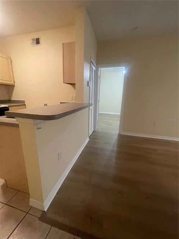 A kitchen with a breakfast bar overlooks a living area with wood-look flooring — 8820 DUNES COURT UNIT 202, KISSIMMEE, FL