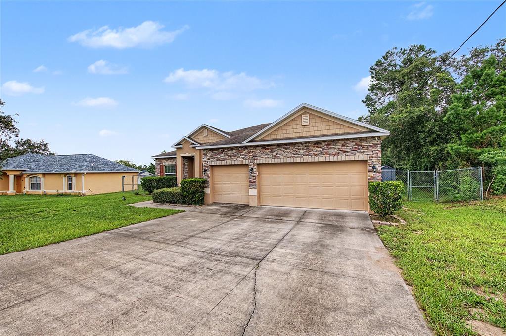 A single-story house with a stone facade, tan garage doors, and a concrete driveway — 6545 LANDOVER BOULEVARD, SPRING HILL, FL