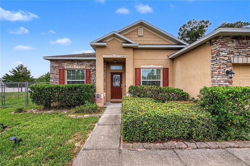 A tan single-story house features stone accents, brown shutters, and a front walkway — 6545 LANDOVER BOULEVARD, SPRING HILL, FL
