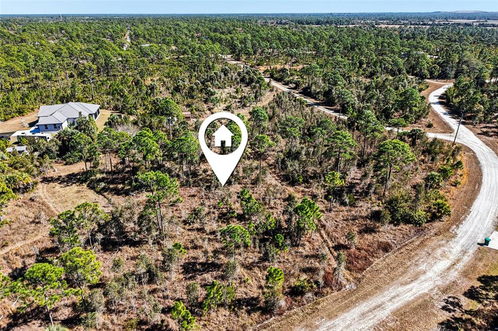 An aerial view shows a wooded, undeveloped lot with a house nearby and a dirt road — 13592 CAROUSEL DRIVE, PUNTA GORDA, FL