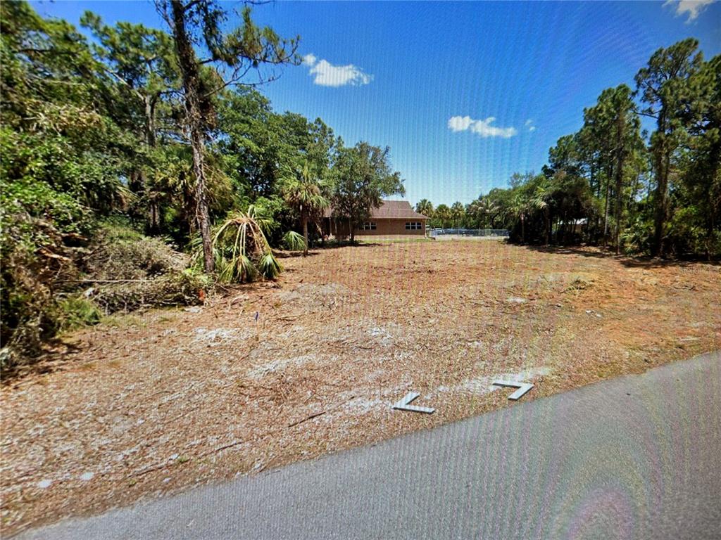 A vacant, cleared residential lot sits next to a paved road with trees in the background — 1412 LULLABY STREET, PORT CHARLOTTE, FL