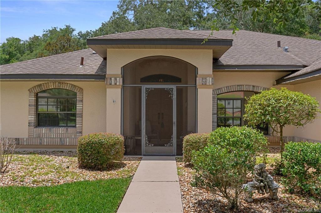 A single-story house with a beige stucco exterior, arched windows, and a screened front entryway — 3116 N STRATHAM POINT, HERNANDO, FL