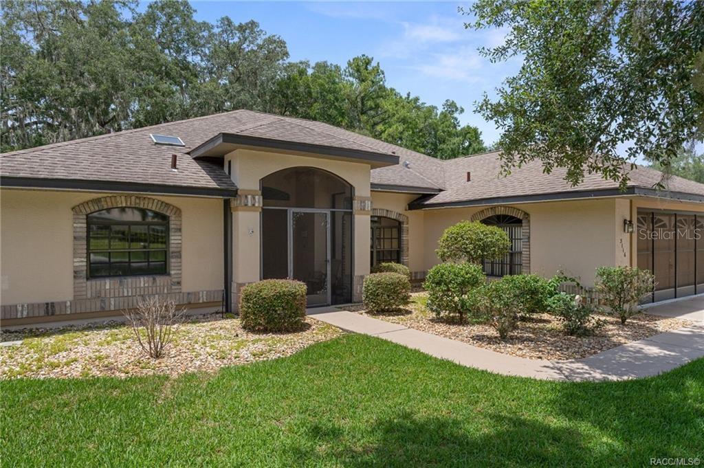 A single-story house with a tan stucco exterior, brick accents, and a screened front entryway — 3116 N STRATHAM POINT, HERNANDO, FL
