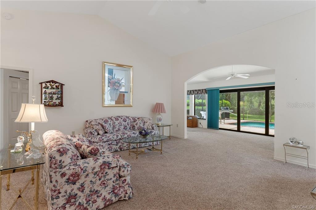 A living room with floral sofas, a vaulted ceiling, and a view of a pool — 3116 N STRATHAM POINT, HERNANDO, FL