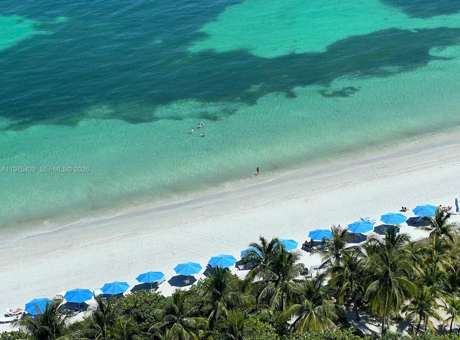 An aerial view shows a white sand beach with blue umbrellas and turquoise water — 881 Ocean Dr, Key Biscayne FL 33149, KEY BISCAYNE, FL
