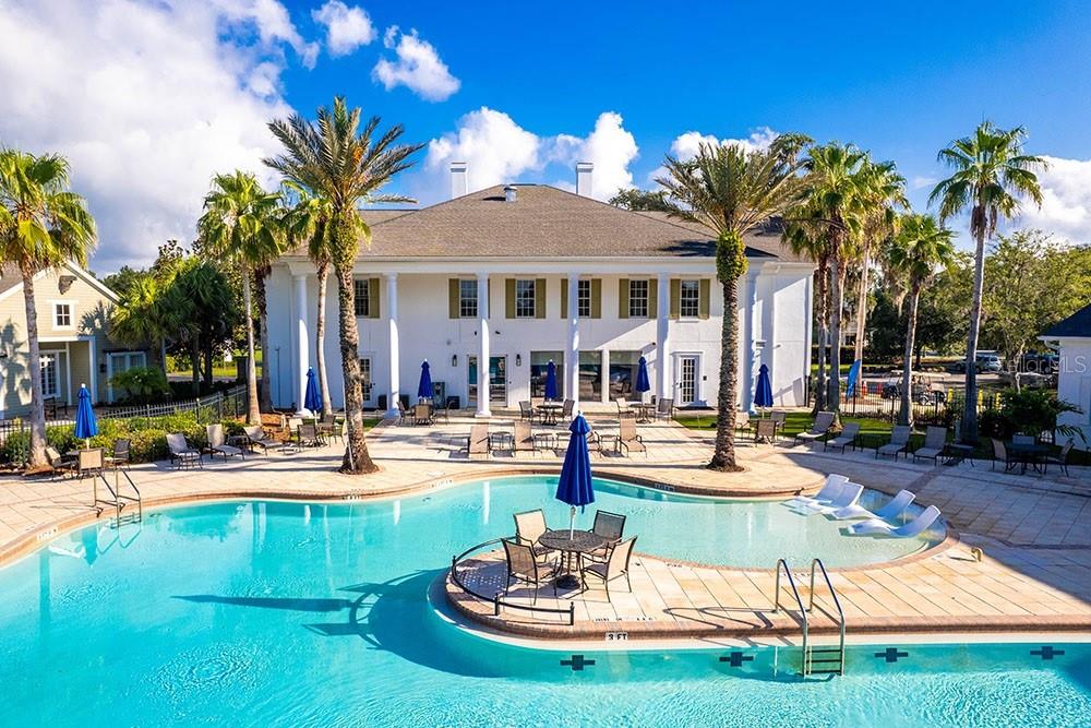 A swimming pool with a central seating area sits in front of a white building — 6156 DUSK ROSE LANE, BROOKSVILLE, FL