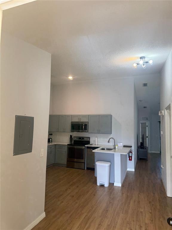 A kitchen with gray cabinets, stainless steel appliances, and wood-look flooring opens to a hallway — 2774 CLUB CORTILE CIR UNIT B, KISSIMMEE, FL