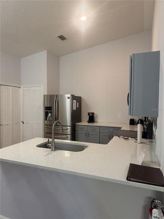A kitchen features a stainless steel refrigerator, gray cabinets, and a white quartz countertop island — 2774 CLUB CORTILE CIR UNIT B, KISSIMMEE, FL