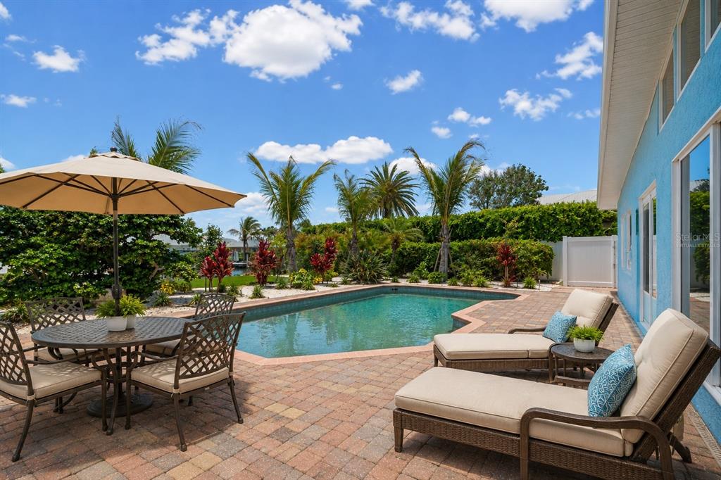 A patio with a pool, lounge chairs, and a dining set under a large umbrella — 528 KEY ROYALE DRIVE, HOLMES BEACH, FL