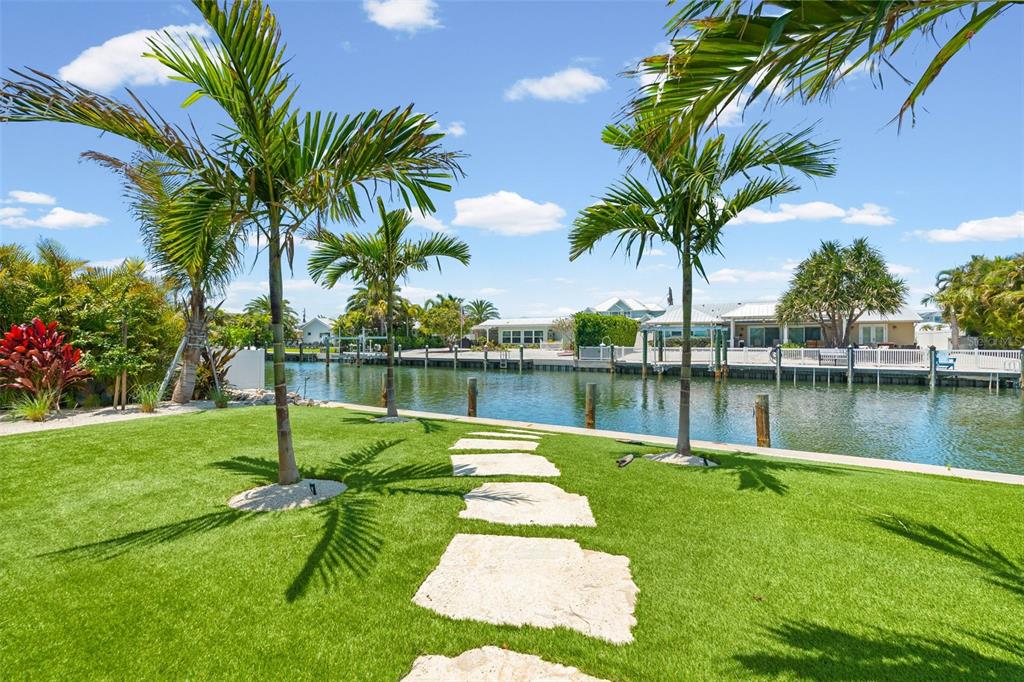 A grassy backyard with palm trees and stone pavers leads to a canal waterfront — 528 KEY ROYALE DRIVE, HOLMES BEACH, FL