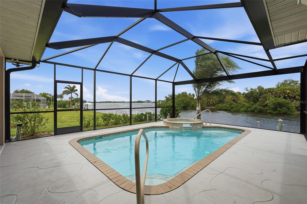 A screened-in pool and hot tub overlook a body of water with a grassy yard — 470 SPRING LAKE BOULEVARD NW, PORT CHARLOTTE, FL