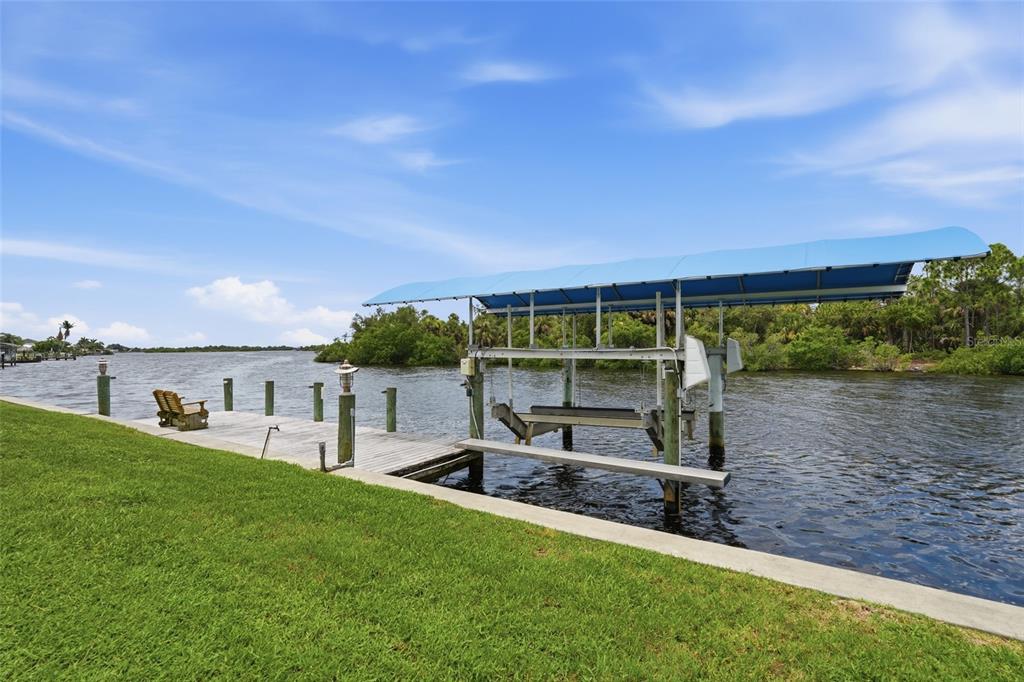 A wooden dock with a boat lift sits along a grassy lawn by the water — 470 SPRING LAKE BOULEVARD NW, PORT CHARLOTTE, FL